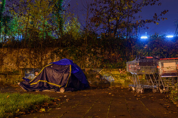 Tent of a homeless person in the city at night, shopping cart and a tent of a homeless person at night, rainy weather