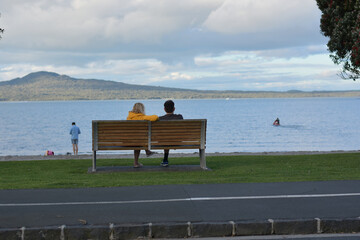 AUCKLAND, NEW ZEALAND - Nov 06, 2020: man and woman sitting on park bench at Tamaki Drive Mission...