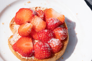 A rusks with strawberries with sugar on a white plate. blue background. Selective focus