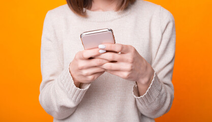 Close up photo of woman hands holding and using smartphone over yellow background