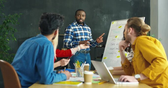Mixed-races group of startuppers having meeting and discussing new project development in office. African American man speak at conference of young multiethnic managers. Male reporting for colleagues.