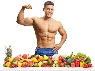 Fototapeta premium Topless muscular man showing flexing biceps muscle and posing with a pile of fruits and vegetables