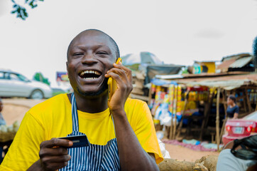 young handsome african trader feeling excited as he makes call with phone while holding his credit card