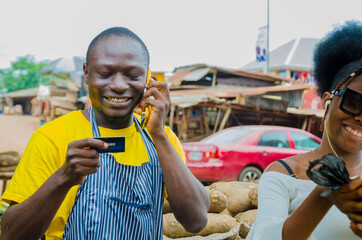 young handsome african trader feeling excited as he makes call with phone while holding his credit card