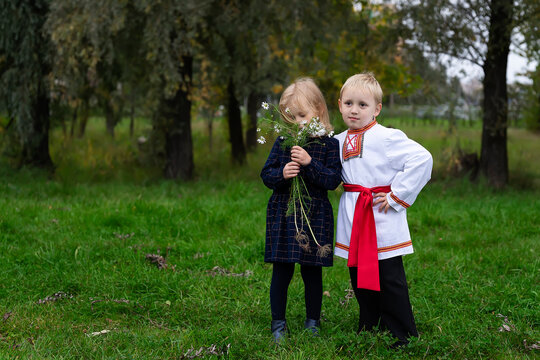 A little boy in old Russian clothes gives chamomile flowers to a girl in a blue dress