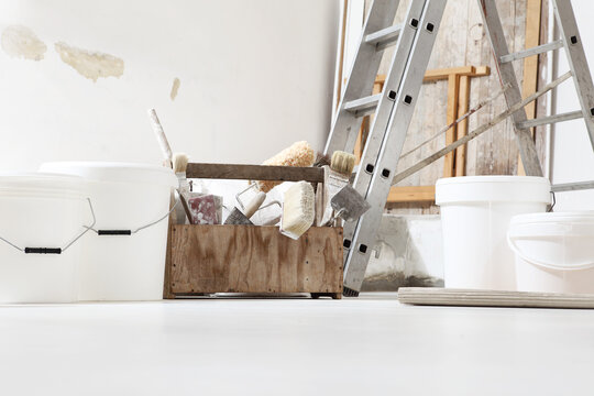 Indoor Shot Close Up Frontal View Of Bricklayer, Plasterer Or House Painter Tools On White Floor With Buckets In Home Renovation Site