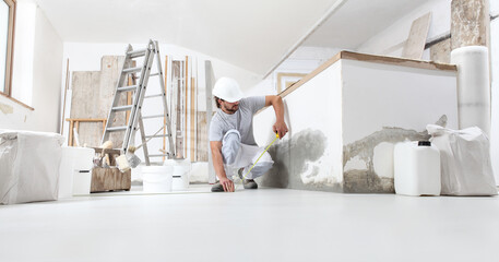 construction worker plasterer man measuring wall with measure tape in building site of home...