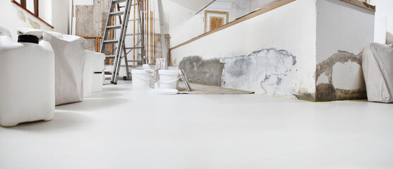 Low angle of indoor shot of construction or building site of home renovation with tools with paint buckets and primer jerry can on white floor with copy space