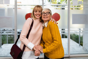 Beautiful middle age woman with her mother visiting hospital or nursing center. They are happily talking and smiling.