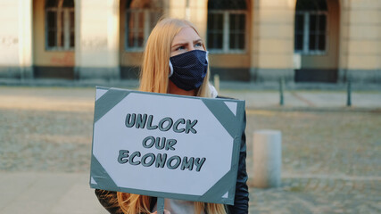 Young woman wearing medical mask calling to unlock the economy by holding steamer. Protest walk in the city center.