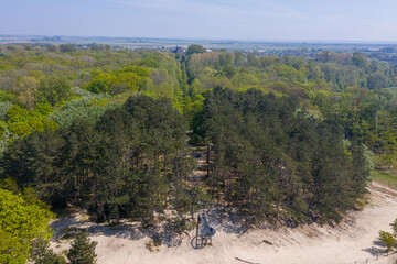 Aerial drone photograph of green deciduous and pine forest near Burgh-Haamstede in Zeeland, Netherlands, with a sandy clearing visible amid dense woodland captured in April 2020 under soft spring ligh