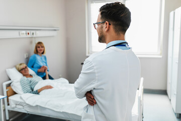 Obraz premium Young doctor visiting sick senior woman with her daughter in hospital room or nursing center.
