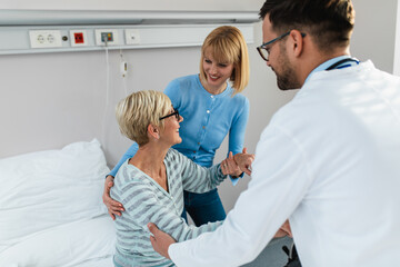 Fototapeta premium Young doctor visiting sick senior woman with her daughter in hospital room or nursing center.