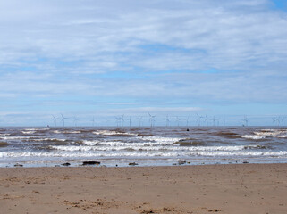 Fototapeta na wymiar the beach at blundell flats in southport with waves breaking on the beach and the wind turbines at burbo bank visible in the distance