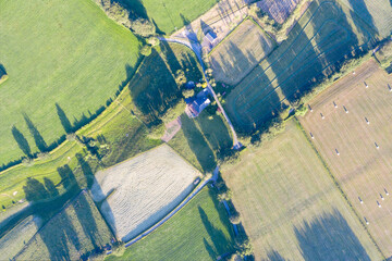 Aerial drone view of patchwork fields and hedgerows around Waimes in the Belgian Ardennes, captured in June 2020. Green meadows, pale crops and blue lanes cast long shadows across the rural landscape.