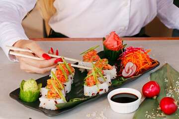 Sushi Roll on a black plate with woman hand holding chopsticks, japanese food