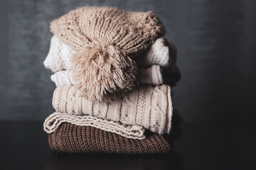 Winter woolen cap on sweaters piles on a desk at home. Clothes for winter and cold day concept. Copy space for design or text