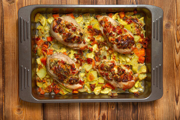 Ready-made chicken fillet on a baking sheet with olives and vegetables on a wooden table, top view, copy space