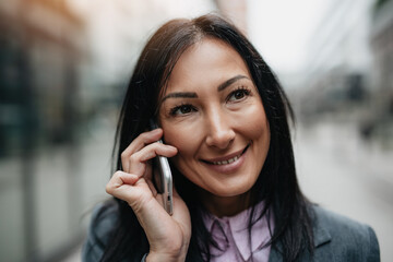 Attractive middle age business woman walking and standing on city street. She is positive and using her smart phone. Modern business building in background.