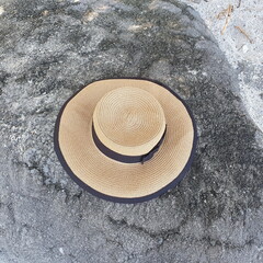 Fototapeta na wymiar A vintage wide-brimmed hat with a black ribbon and a bow attached to the hat rests on the beach rocks. Always wear a hat to protect against UV rays from the sun while outdoors or wear hat for fashion 