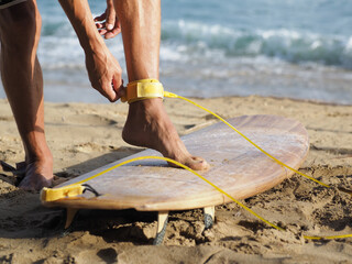 Close-up shot. Surfer putting on a leg yellow leash.