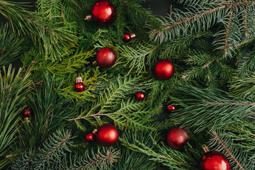 Obraz na płótnie Canvas Creative layout made of evergreen tree branches and red Christmas balls. Winter nature New Year concept. Flat lay, top view, copy space.