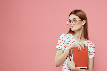 female student with notepads on pink background gesturing with her hands glasses on her face striped t-shirt model