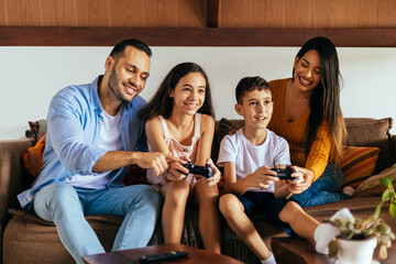 Latin family enjoying the day together at home playing video games on the couch