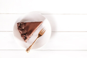 A piece of chocolate cake on a white plate with a gold fork on a white plate. Traditional sweets for birthday and other holidays