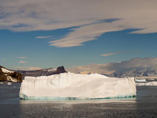 Large white iceberg in Antarctica with land, blue sky and white cloud background