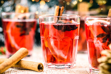 Mulled red wine with spices and Christmas fruits on a rustic wooden table with Christmas colors and lights. Traditional hot drink at Christmas time