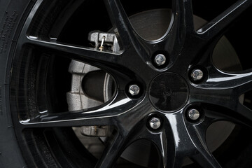 Image of a car tire fitted with black alloy rims  and view of the brakes