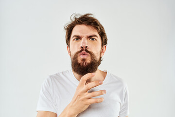 Emotional bearded man in a white t-shirt gestures with his hands light background