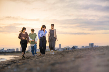 夕暮れの中、寄り添って海沿いを歩く女性4人