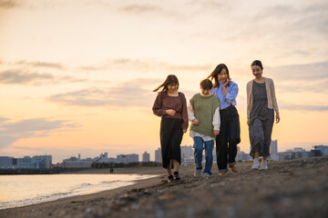Fototapeta premium 夕暮れの中、寄り添って海沿いを歩く女性4人