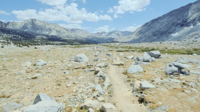 Revealing shot of beautiful rocky terrain with big mountains in the distance and partly cloudy sky (60 fps slowed to 30 fps)