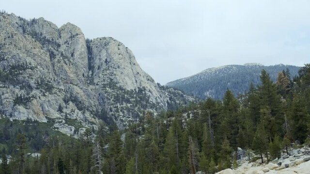 Revealing shot of large rocky mountain surrounded by trees and clouds in the Sierras (60 fps slowed to 30 fps)