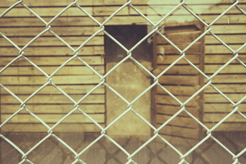 Closeup of metal net with a glass wall and a wooden house behind it. Toned image.