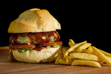Close up of a homemade burger with barbecue sauce on a chopping wood board, on black background