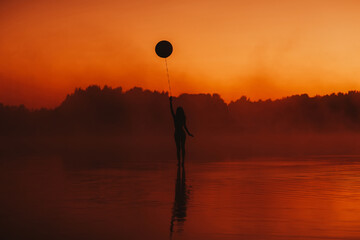 surreal silhouette of a girl with a balloon in her hand on the water