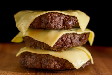 Close up of a homemade burger meat and cheese only on a chopping wood board, on black background