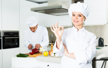 Young female cook in uniform showing ok hand sign on kitchen ....