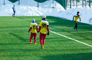 Boys in gray yellow sportswear running on soccer field with snow on background. Young footballers dribble and kick football ball in game. Training, active lifestyle, sport, children winter activity