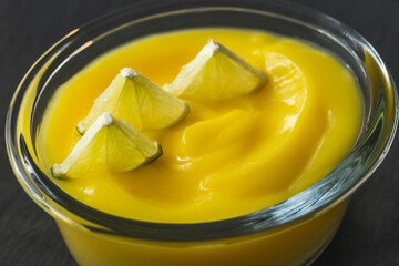 Lemon pudding in a glass bowl served with sliced lemon extremely close up