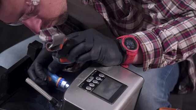 Trying to fix coffee machine. Service and repair of coffee maker. Adult handyman repairing coffee machine by screwdriver at home. Male mend percolator in goggles and black rubber gloves