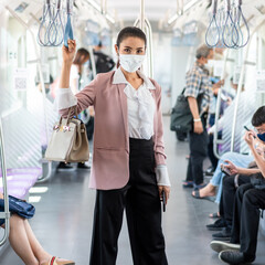 Asian business woman travelling on train in city wearing mask and pink blazer