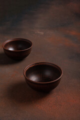 Two dark handmade clay bowls on brown background