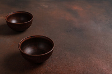 Two dark handmade clay bowls on brown background