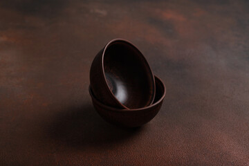 Two dark handmade clay bowls on brown background