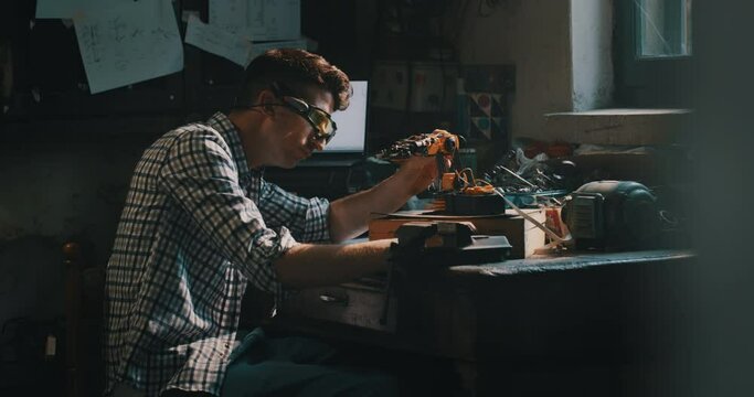 Cinematic shot of an young professional engineer with specific glasses is working on projection of an innovative technology mechanical arm in his workshop.